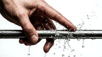 Male hand touching water pipe with droplets splashing against white background isolated for plumbing repair maintenance design concepts.