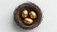 Three golden eggs nestled in natural brown twigs nest against light background, symbolizing wealth, investment growth and financial security.