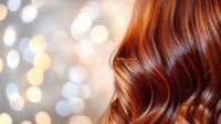 Luxurious copper red wavy hair on blurred bokeh background. Professional hairstyling with soft waves and highlights showcasing healthy, shiny hair texture.