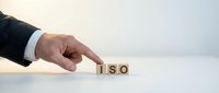 Businessman hand pointing at wooden blocks spelling ISO on white surface for business compliance and standards concept.