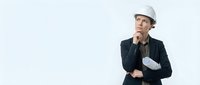 Thoughtful male engineer or architect wearing hard hat and dark blazer holding blueprints, isolated on white background for business and construction design projects.