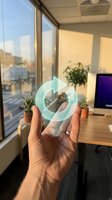 Hand holding transparent recycling symbol in modern office environment with city view through windows promoting environmental sustainability in workplace.