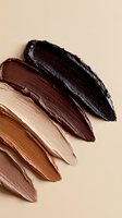 Makeup foundation swatches in different skin tone shades from light to dark brown on beige background, showing creamy texture and smooth application strokes.