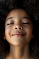 Young person with curly hair and closed eyes expressing serenity and joy, face illuminated against dark background, showing genuine smile and peaceful expression.