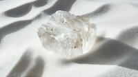 Raw transparent crystal on white silk fabric with soft shadows creates ethereal minimalist composition for wellness, spirituality and luxury designs.