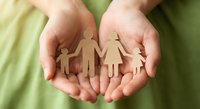 Hands holding paper cutout family figures representing protection, care, insurance, adoption, social services, community support and family planning concepts.