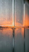 Close-up of frosted glass window panes with warm orange sunset light filtering through condensation droplets creating atmospheric mood for interior design.