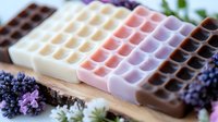 Handmade soap bars with waffle pattern texture in pastel and chocolate colors arranged on wooden surface with lavender flowers, spa and wellness concept.