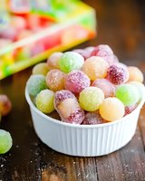 Colorful sugar-coated gummy candies in white ceramic ramekin on wooden table. Round fruit-flavored sweets in assorted pastel colors with crystalline coating.