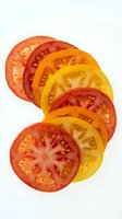 Sliced heirloom tomatoes in red, orange and yellow varieties arranged in overlapping rows on white background, isolated for culinary and food design use.