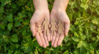 Hands holding wooden family figures over green grass background representing protection, care and unity concepts for insurance and social services.