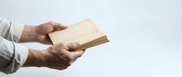 Elderly hands holding open vintage book against white background for reading and literature concepts.