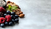 Fresh organic blueberries, raspberries, almonds, chia seeds and mint leaves arranged on light gray background with copy space for healthy breakfast concept.