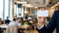 Businessman holding blank white card in modern office with colleagues working in background, corporate environment for business communication and branding.