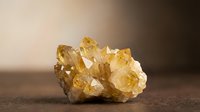 Cluster of golden yellow citrine crystals with natural terminations and translucent facets on neutral surface for mineral collection, geology education, and wellness product photography.