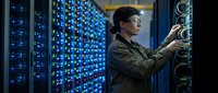 Female IT technician working with server cables in modern data center with blue LED lights maintaining network infrastructure equipment.