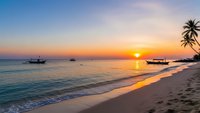 Tropical beach sunset with golden sky reflecting on calm ocean waves, traditional boats anchored offshore, palm tree silhouette and pristine sandy shore.