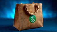 Eco-friendly brown jute shopping bag with rope handles and green leaf logo tag against dramatic blue background, promoting sustainability and zero waste lifestyle.