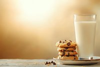 Stack of fresh chocolate chip cookies on rustic plate with cold glass of milk against warm golden background, classic comfort food styling on wooden table.