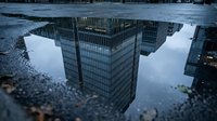 Modern skyscrapers reflected in urban puddle after rain, creating inverted cityscape view. Use for architecture, urban design, real estate, and contemporary city concepts.