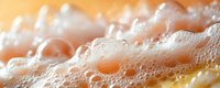 Macro shot of soap bubbles and foam texture with golden liquid beneath creating abstract pattern of spheres and light reflections in warm tones.