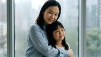 Asian mother and daughter embracing by window in modern home, showing family love and bonding moment between parent and child in natural light setting.