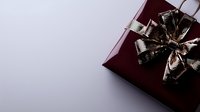 Elegant burgundy gift box with metallic silver bow on light background, corner composition with copy space for holiday and celebration designs.