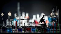 Chemistry laboratory equipment with colorful liquids in glass beakers, flasks and test tubes on dark background for scientific research and education.