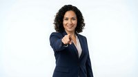 Professional Hispanic businesswoman in navy suit pointing forward with confident smile on white background for corporate presentations.