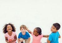 Young children laughing together outdoors, featuring diverse group of boys and girls in casual colorful clothing, expressing joy and friendship during playtime.