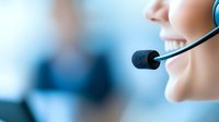 Smiling female customer service representative wearing headset in office environment, close-up view showing professional communication and positive attitude.