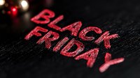 Red glowing text Black Friday on dark textured background with bokeh lights, closeup macro shot of promotional sale lettering for retail marketing.