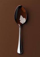 Elegant silver spoon with reflective surface against rich brown background, showcasing minimalist tableware design for food photography and culinary presentations.