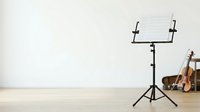 Young adult male musician of mixed ethnicity arranging sheet music on a stand in a bright studio space with violin and cello nearby, suitable for music education, lessons, and creative projects.