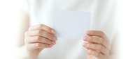 Woman in white sweater holding blank white card with both hands against soft neutral background for mockup and branding projects.