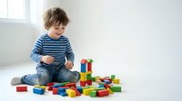Young boy in striped shirt playing with colorful wooden building blocks on floor, developing motor skills and creativity through educational toy construction.