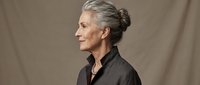 Mature woman with gray hair in bun, wearing black shirt, profile view against neutral beige background. Suitable for business, healthcare, education, and corporate website use.