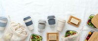 Eco-friendly takeout containers with reusable coffee cups and fresh salad boxes arranged on white surface for sustainable food packaging and zero waste lifestyle concepts.