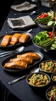 Grilled salmon fillets with fresh vegetables and pasta salad arranged on elegant dark table setting for healthy dining and meal preparation.