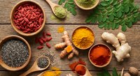Superfood ingredients with goji berries, turmeric, chia seeds and fresh herbs arranged on rustic wooden background for healthy cooking and nutrition.