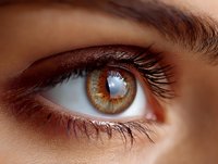 Close-up of amber brown eye with long eyelashes showing intricate iris details and natural light reflection, suitable for vision care advertising.