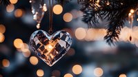 Crystal heart ornament hanging on Christmas tree branch with warm bokeh lights creating romantic holiday atmosphere. Perfect for seasonal decorative designs.