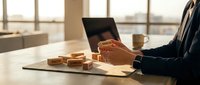 Businessman in dark suit holding wooden blocks on office desk with laptop and coffee cup, representing business growth, strategy planning, and corporate development in modern workplace.