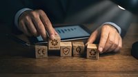 Businessman hands arranging wooden cubes with quality control and certification symbols on desk with laptop in background for compliance management.