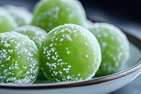 Green Japanese mochi dessert balls dusted with powdered sugar on white ceramic plate, close-up macro shot showing soft texture and traditional confection details.
