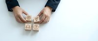 Business professional arranging wooden blocks with question marks and gears symbols on white desk representing problem solving and strategic thinking.