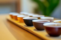 Traditional tea ceremony with ceramic cups arranged in row on wooden tray, selective focus creates soft bokeh effect, warm ambient lighting enhances mood.