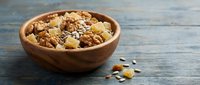 Wooden bowl filled with mixed nuts, seeds, and dried fruits on a rustic blue wooden table, healthy snack concept for nutrition blogs.
