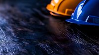 Construction safety helmets in orange and blue colors arranged on dark textured background with dramatic lighting and selective focus for workplace safety concept.