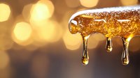 Golden honey drips from glass surface against warm bokeh background, creating luxurious drops and streams in macro photography with natural amber glow.